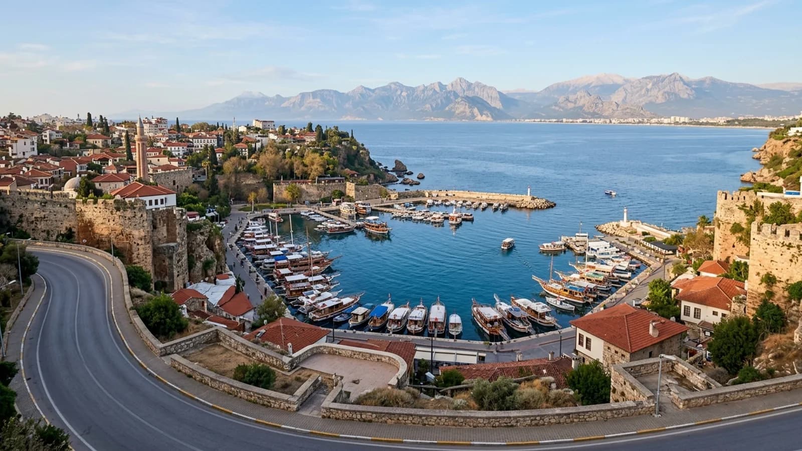Book a Lara taxi transfer to Kaleiçi to see the old harbour, moored wooden boats, historic houses, and distant mountains.